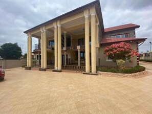 A building with a covered entrance, multiple columns, a balcony, and a red roof. - Cozy Kumasi Apartment With 2 Bedrooms (Kumasi)