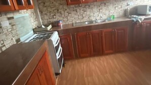 A kitchen with wooden cabinets, a tiled backsplash, and a ceiling fan. - Cozy Kumasi Apartment With 2 Bedrooms (Kumasi)