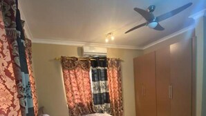 A bedroom with a bed, curtains, a ceiling fan, and a wardrobe. - Cozy Kumasi Apartment With 2 Bedrooms (Kumasi)