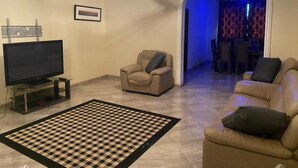 A living room with a flat-screen TV, two sofas, a patterned rug, and a ceiling fan. - Cozy Kumasi Apartment With 2 Bedrooms (Kumasi)