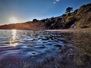 On peut admirer une vue dégagée sur un lac, où la lumière du soleil se reflète à la surface de l’eau. Le lac est bordé d’une rive rocheuse et d’une végétation clairsemée.