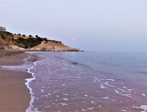 Une plage bordée d’une falaise rocheuse et baignée par une mer calme.