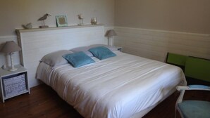 A bedroom with a bed, two bedside lamps, a nightstand, a chair, and a shelf with decorative items. - Landes house 10 min from the beach, 5min from the cycle path and forest (Mimizan)