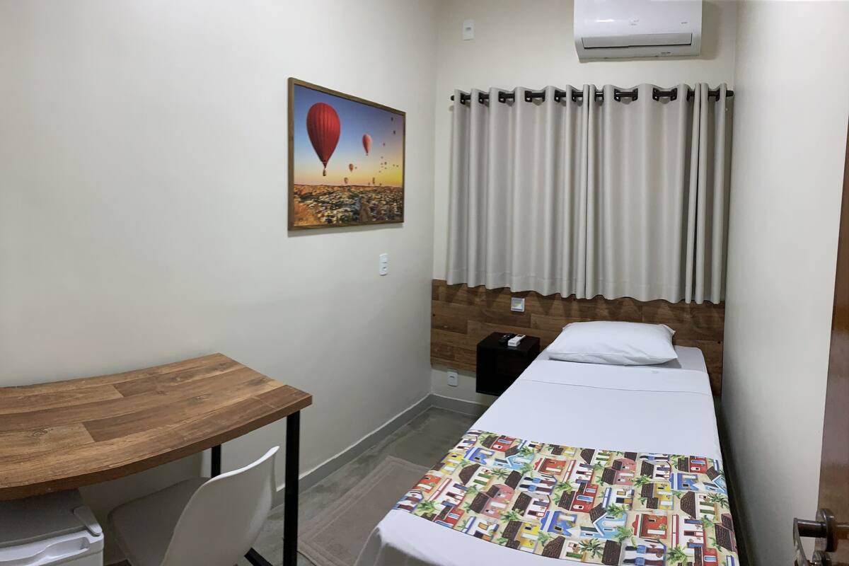 Habitación de hotel con escritorio de madera, cama con colcha colorida, pintura de globos aerostáticos en la pared y ventana con cortinas.