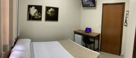 A bedroom with a bed, a desk with a laptop, a TV, and two framed floral pictures on the wall.