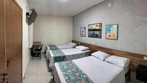 Ein Hotelzimmer mit drei Einzelbetten, einem Schreibtisch und einem an der Wand befestigten Fernseher.