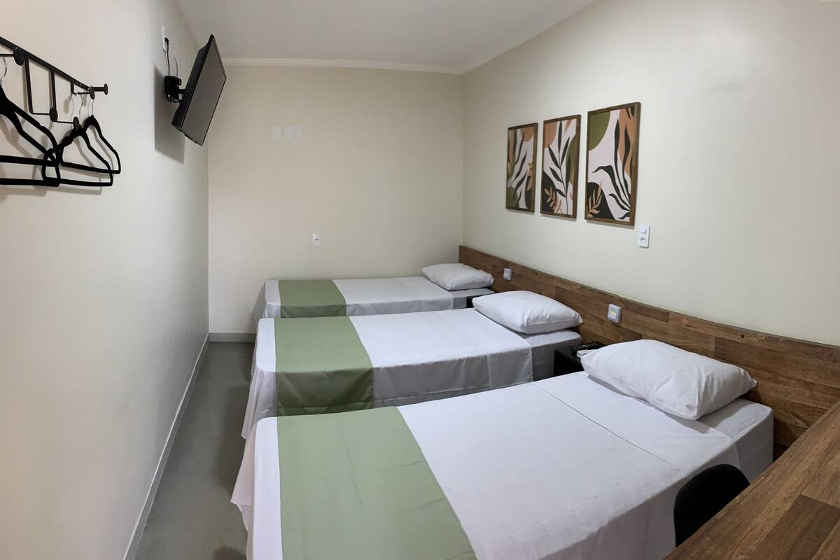 Una habitación con tres camas individuales, cabecero de madera, televisor de pantalla plana montado en la pared y tres cuadros enmarcados sobre las camas.