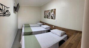 Ein Zimmer mit drei Einzelbetten, einem Holzkopfstück, einem flachbildfernseher an der Wand und drei gerahmten Kunstwerken über den Betten.