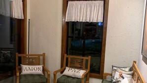 Ein gemütliches Zimmer mit zwei Holzstühlen, einer gepolsterten Bank und einem Fenster mit weißem Vorhang.