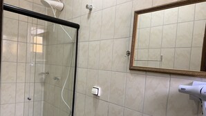 Ein Badezimmer mit Duschkabine aus Glas, Waschbecken mit Spiegel und Fön auf der Ablagefläche.