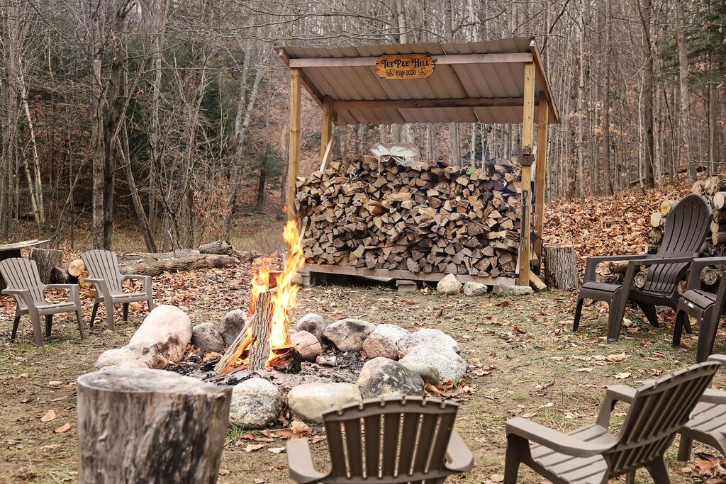 A campfire with chairs around it, a pile of firewood, and a sign that reads "Teepee Hill".