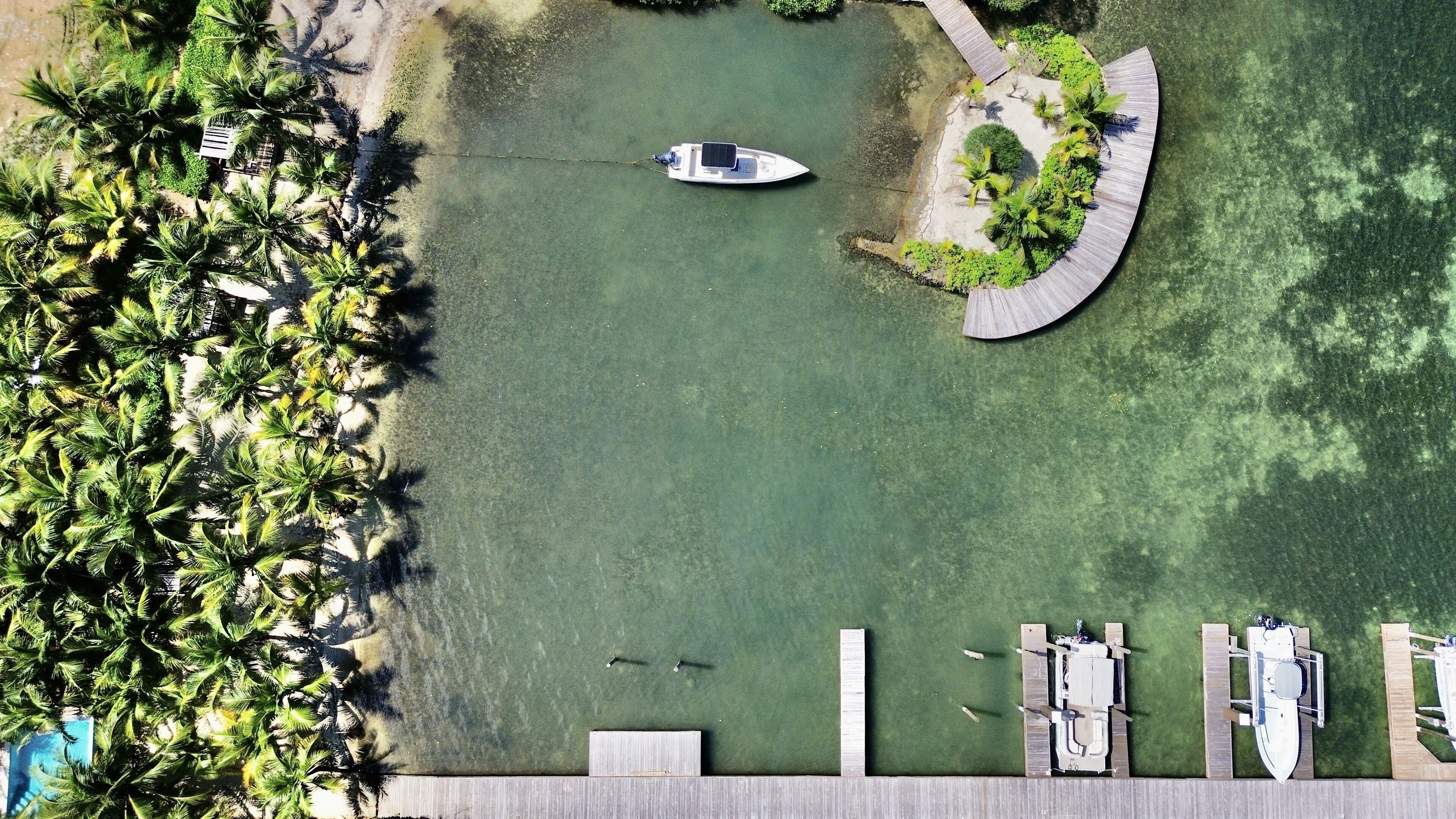 Eine Luftaufnahme einer Marina mit vertäuten Booten, umgeben von Palmen und einer kleinen Insel mit einem gewundenen Steg.