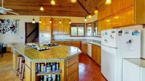 A kitchen with wooden cabinets, a granite countertop island, and hanging pendant lights.