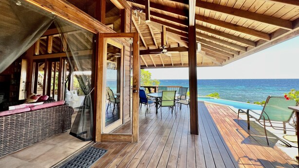 A wooden deck with outdoor seating, a pool, and a view of the ocean.