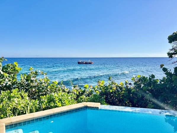 A clear view of a swimming pool with a view of the ocean and a boat in the distance.