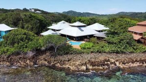 A coastal property with multiple buildings, a swimming pool, and lush greenery.
