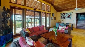 A spacious living area with a wooden ceiling, large windows, and a dining table.
