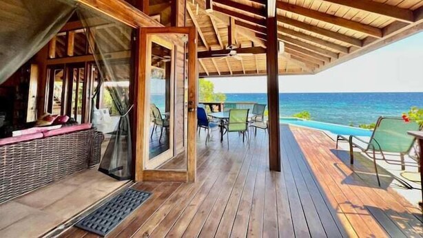 A wooden deck with a covered seating area, a pool, and a view of the ocean.
