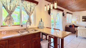 Una cocina con encimeras de granito, armarios de madera, un lavabo de acero inoxidable y un amplio ventanal con cortinas.