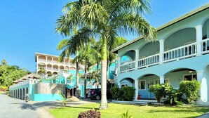 Un hotel de dos plantas con varios balcones y un césped cuidado con palmeras.