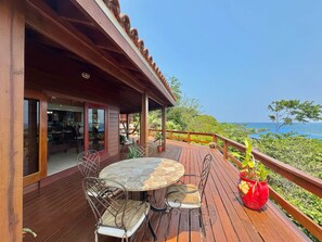 A wooden deck with a table and chairs, a red flower pot, and a view of the ocean. - Villa con Vista @ Calabash Bight, Roatan. (Oakridge)