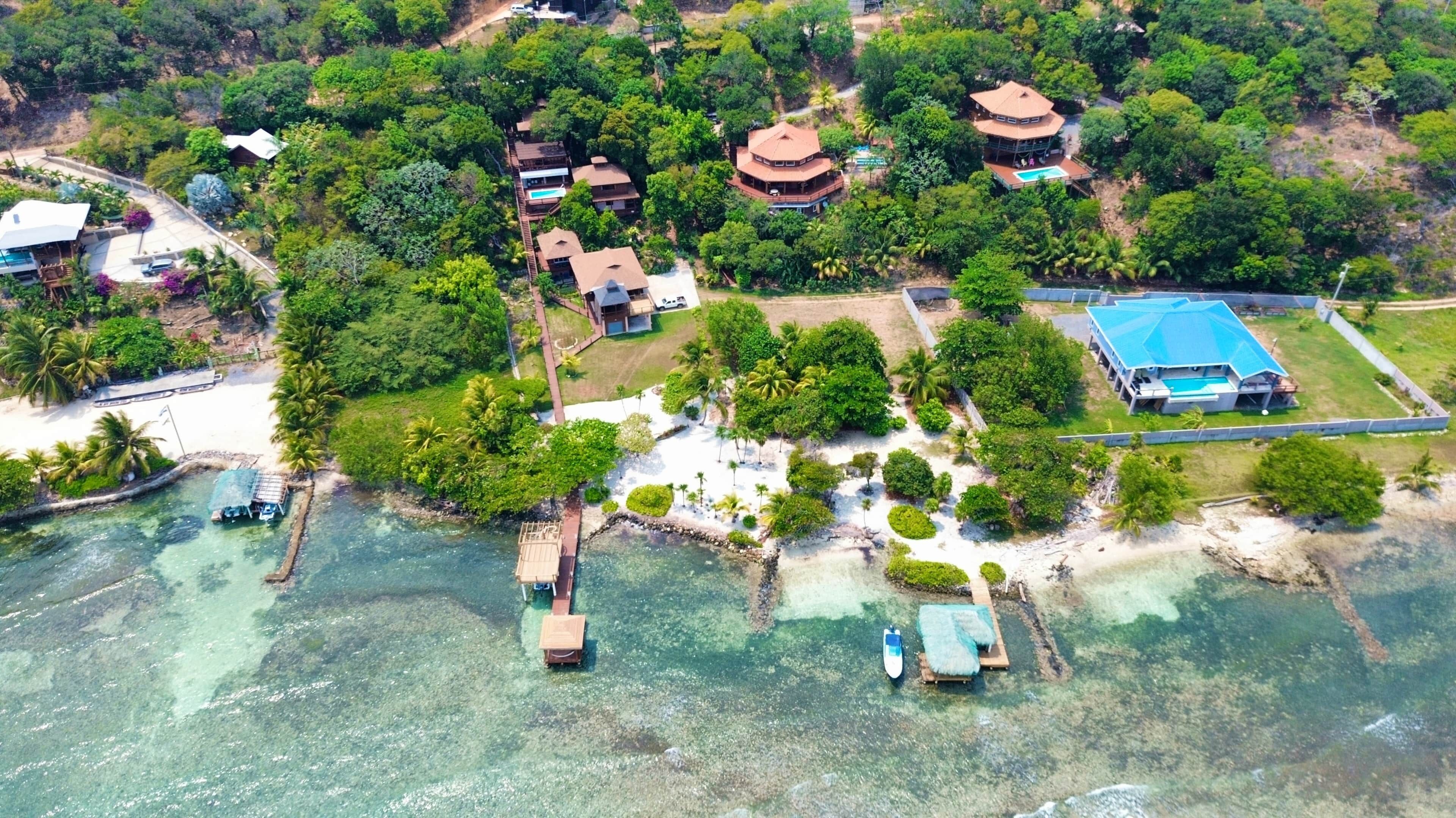 An aerial view of a coastal resort with multiple bungalow-style buildings, a swimming pool, and clear turquoise waters.