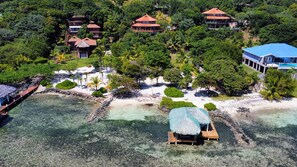 An aerial view of a resort with multiple buildings, a beach, and a thatched-roof structure. - Villa con Vista @ Calabash Bight, Roatan. (Oakridge)
