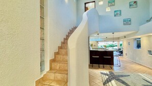 Un interior espacioso con una escalera curva, una zona de comedor con taburetes de bar y vistas al exterior.