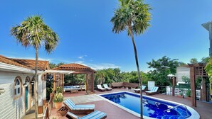 Zona de piscina con sillas de descanso, una pérgola y un pequeño jardín.
