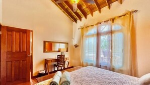 Una habitación de hotel con techo de madera, una cama con colcha estampada, un escritorio con silla y una ventana con cortinas.