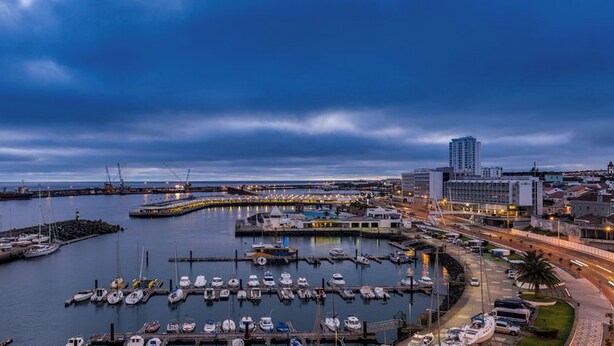 A marina with boats docked, a large building, and a bridge in the background.