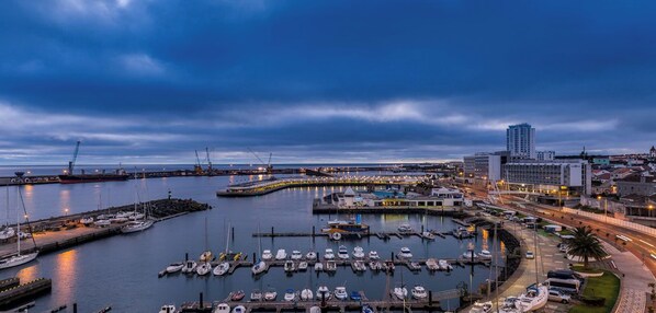 A marina with boats docked, a large building, and a bridge in the background.