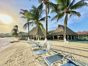 A beachside resort with thatched-roof huts, lounge chairs, and palm trees.