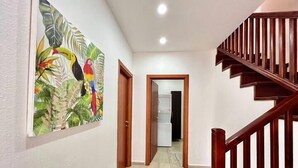 A hallway with a wooden staircase, a door leading to a laundry room, and a colorful painting on the wall. - Turtle Villa 0120 @ Las Palmas Beach, Dixon Cove (Dixon Cove)