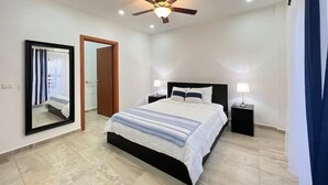 A bedroom with a bed, bedside tables, a ceiling fan, and a mirror. - Turtle Villa 0120 @ Las Palmas Beach, Dixon Cove (Dixon Cove)