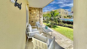 A balcony with white chairs and a table, a stone wall, and a view of a swimming pool and buildings. - Turtle Villa 0120 @ Las Palmas Beach, Dixon Cove (Dixon Cove)