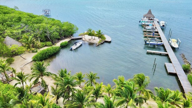 Uma praia tropical com um píer, barcos e uma cabana de palha.