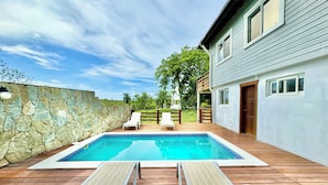 Piscina com duas espreguiçadeiras e um muro de pedra.