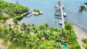 Um resort tropical com um píer, barcos e uma piscina rodeada por palmeiras.