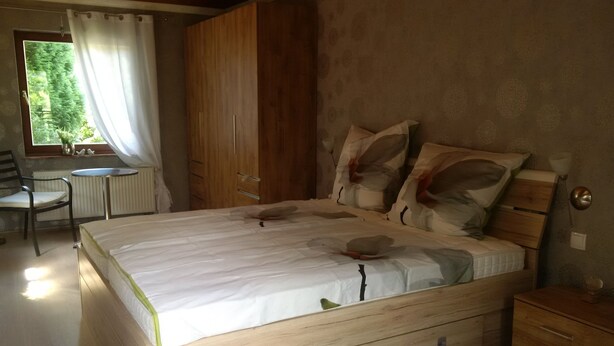 A bedroom with a wooden bed, a small table, and a chair. - House Bergrose (Busenborn)