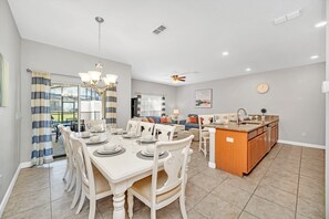 Un comedor amplio con una gran mesa dispuesta para seis comensales, una cocina con isla central y una sala de estar con sofá y mesa de centro.
