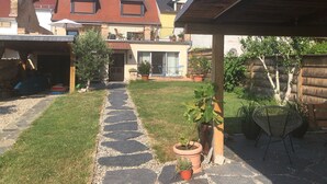 Un patio trasero con un camino de piedra que lleva a una casa. Hay plantas en macetas y un pérgola de madera.