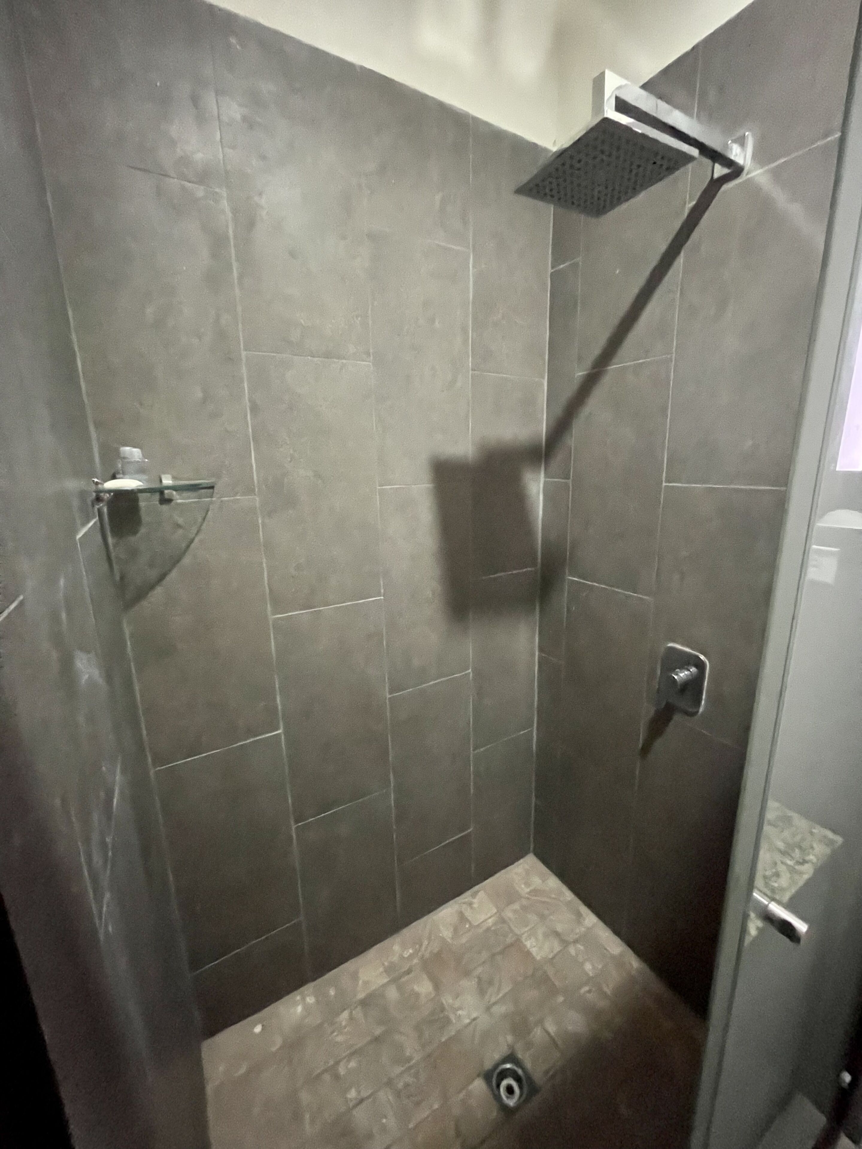 A shower with a glass door and a metal handle, tiled walls, and a drain in the floor.