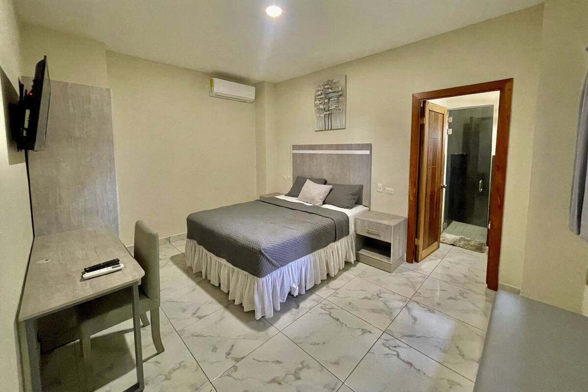 Un dormitorio con una cama, mesitas de noche, un escritorio y un televisor montado en la pared.