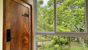 Una habitación con una puerta de madera que dice "305", un ventanal con vista a un jardín y un piso de baldosas.