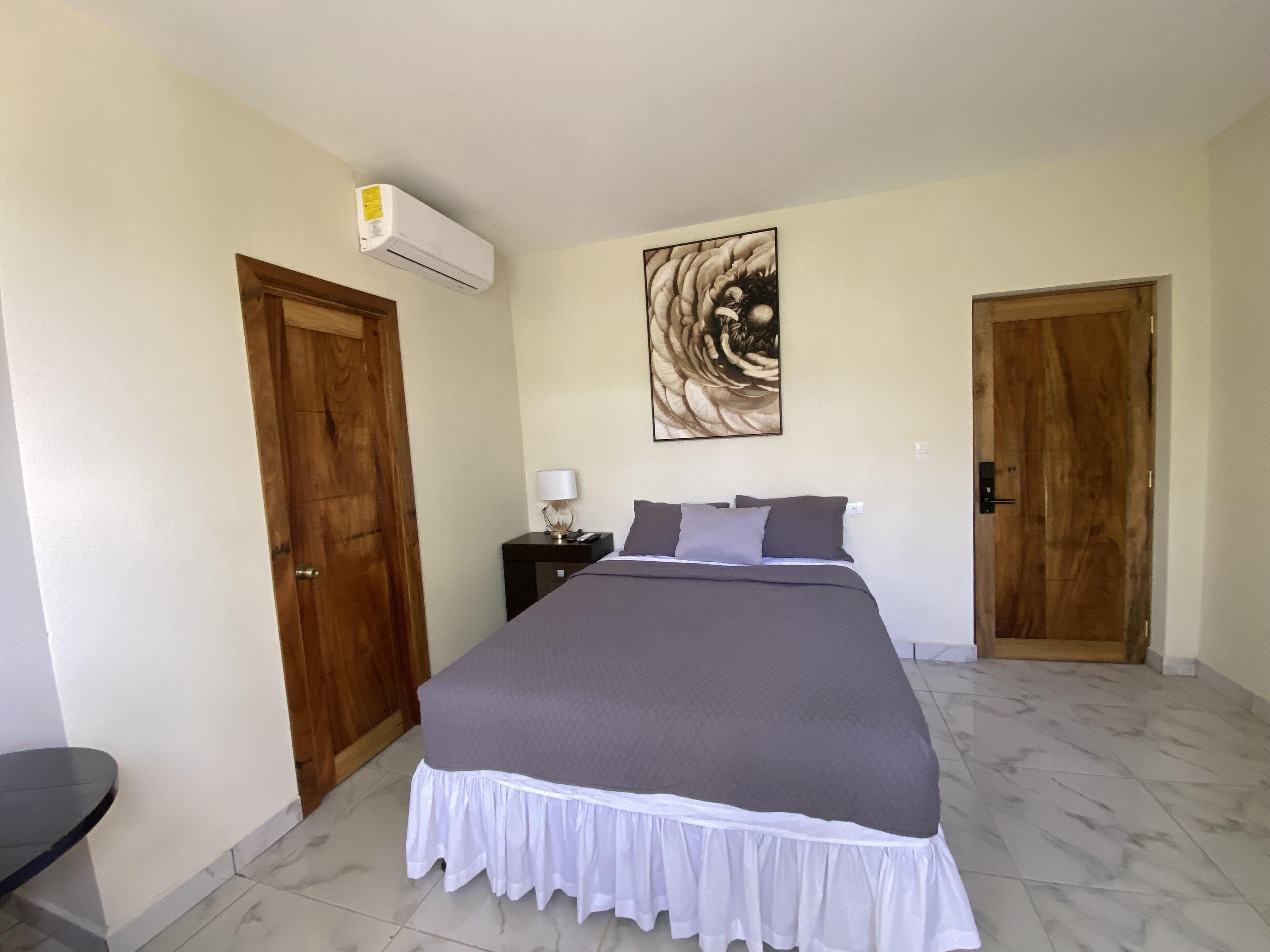 A bedroom with a bed, a nightstand, an air conditioner, and two wooden doors.