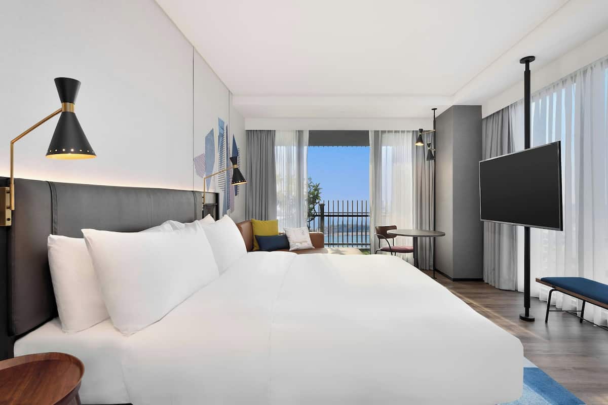 Quarto de hotel moderno com uma cama grande, televisão, escrivaninha e varanda com vista.