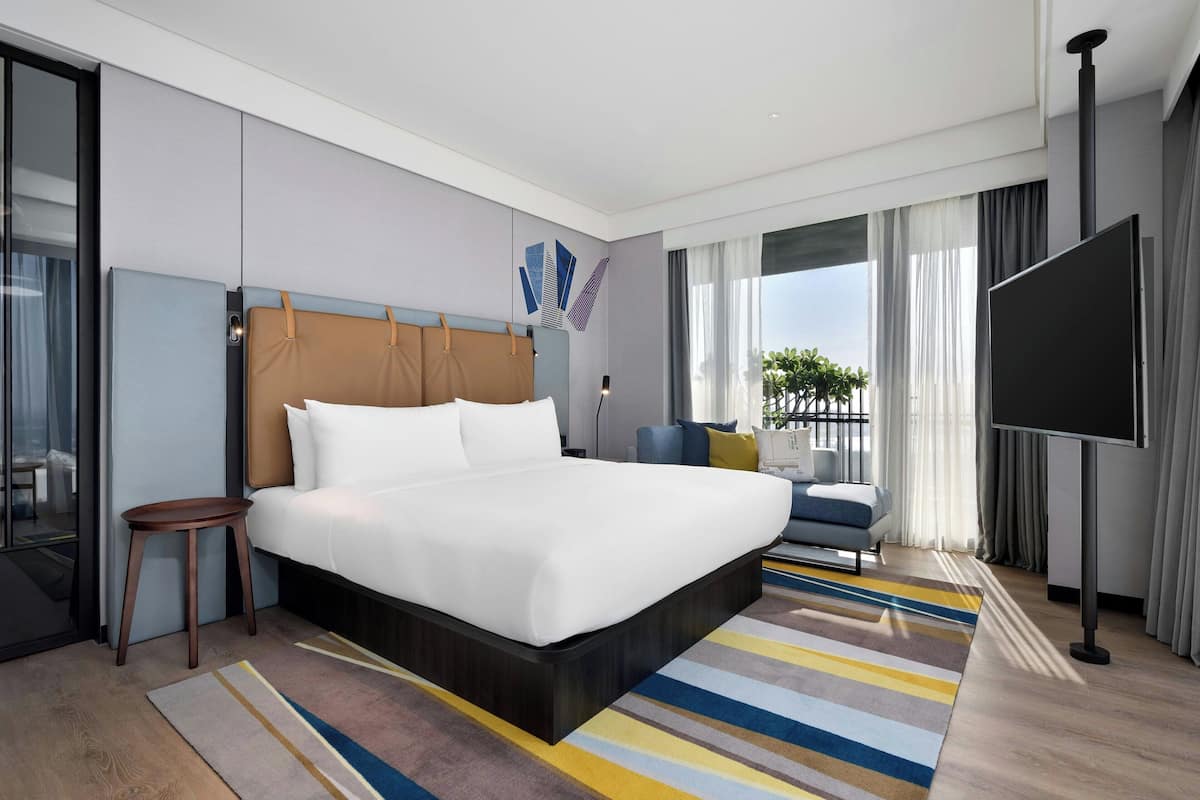 Quarto de hotel moderno com uma cama grande, uma mesa de cabeceira pequena, uma televisão e vista para o exterior.