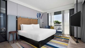 A modern hotel room with a large bed, a small side table, a TV, and a view of the outdoors.