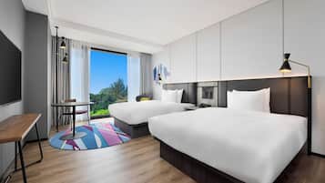 A modern hotel room with two beds, a desk, and a view of the outdoors.